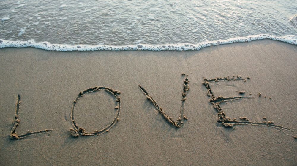 Sur le sable, au bord de l'eau le mot love est dessiné